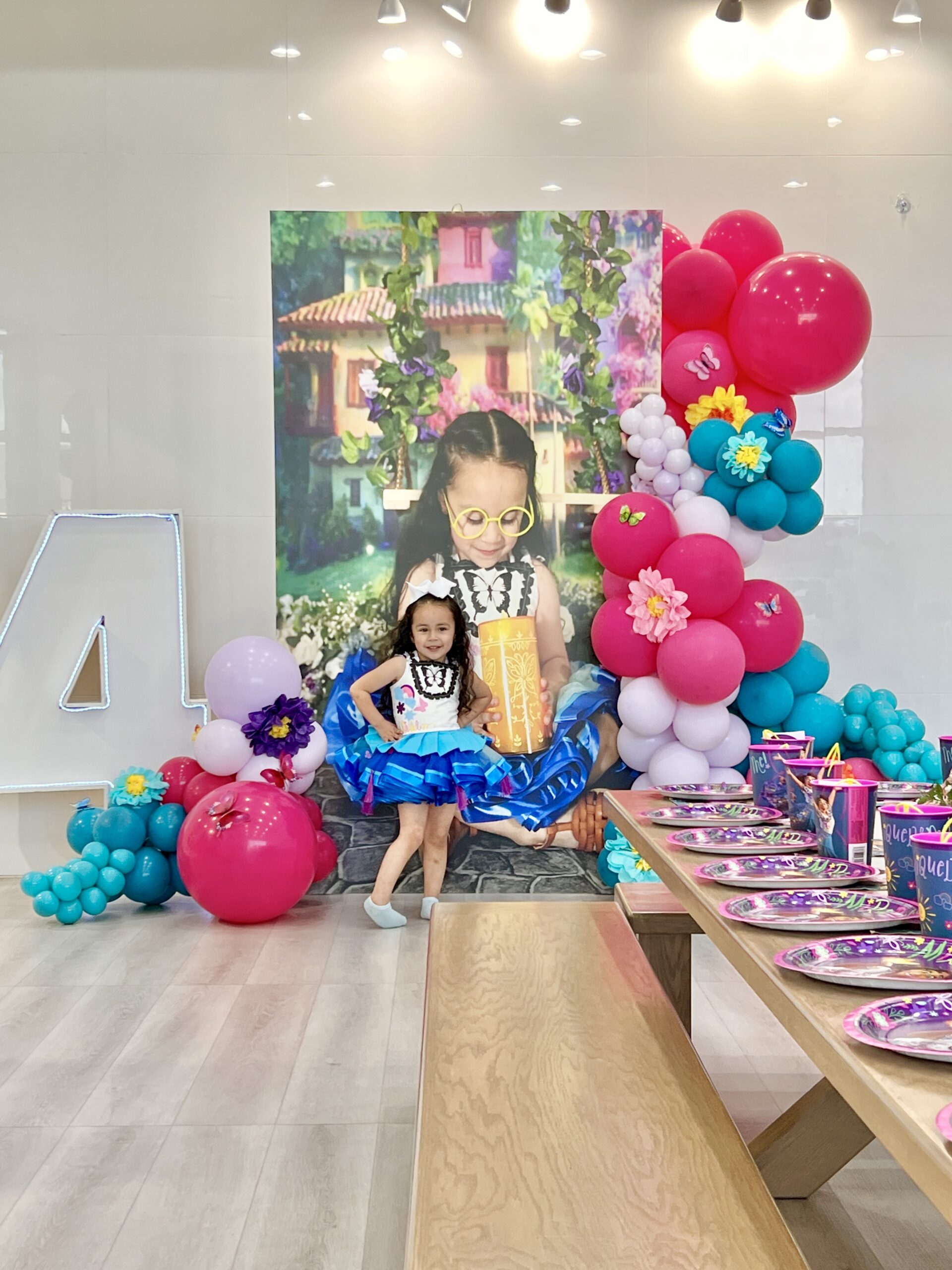 A young girl poses in a colorful party setting with balloons and a festive table