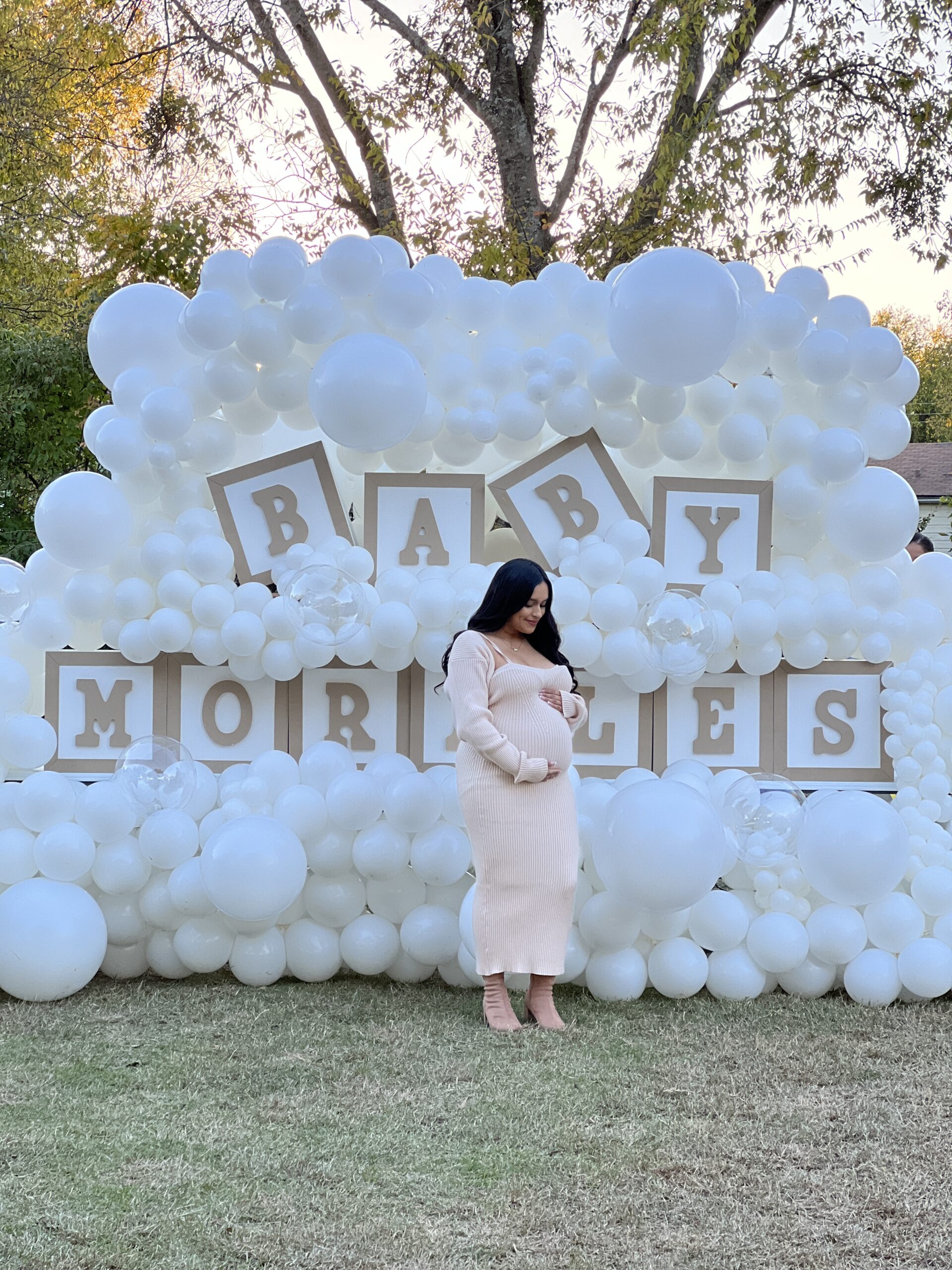 Expectant mother poses in front of a festive balloon display, showcasing "Baby Morles," celebrating an upcoming arrival.