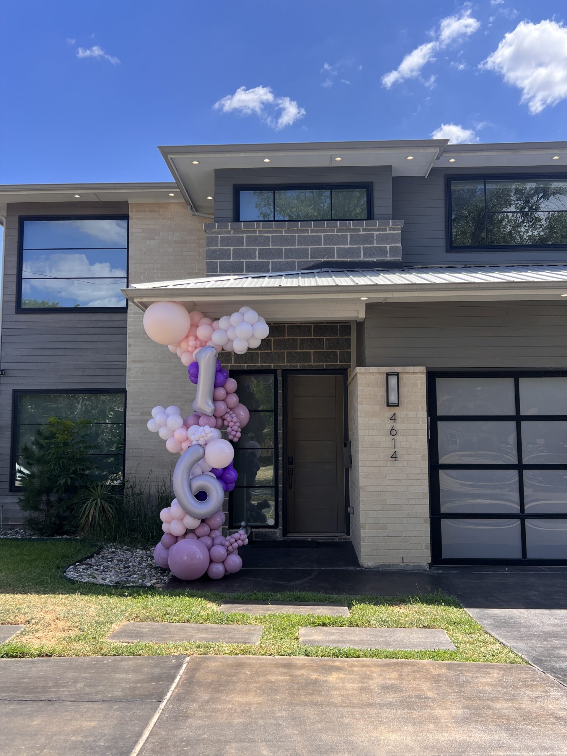 A decorative balloon arch in shades of pink and purple marks the entrance of a modern house, celebrating a 16th birthday.