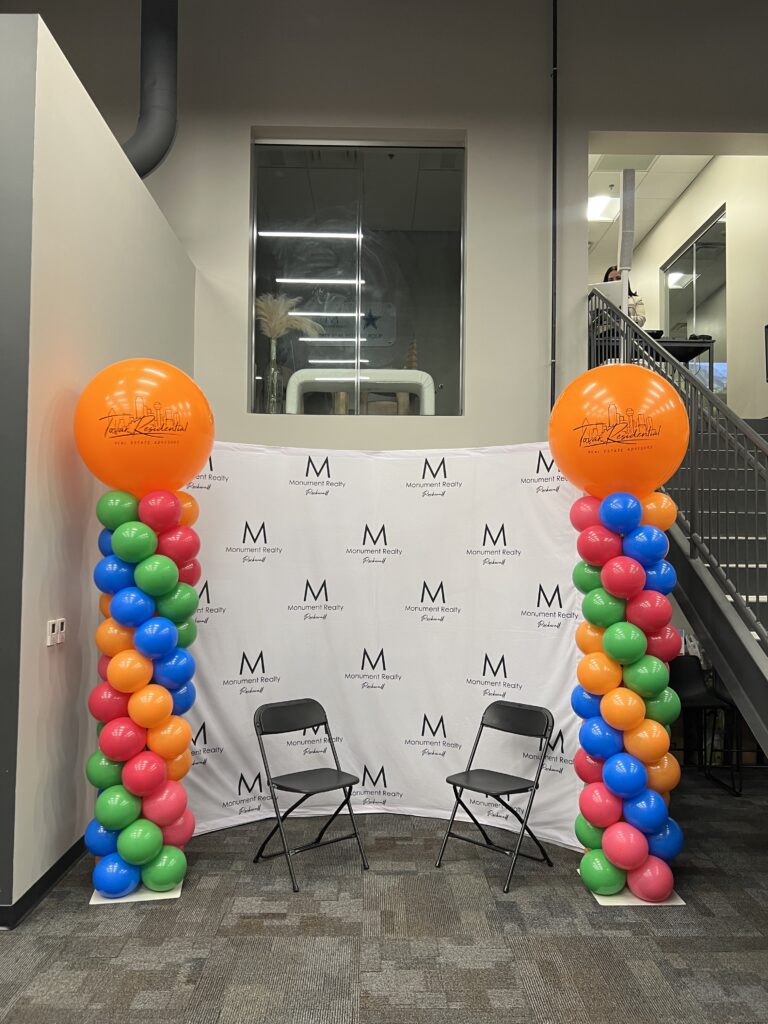 Colorful balloon arch with two black chairs set up in a modern space for an event