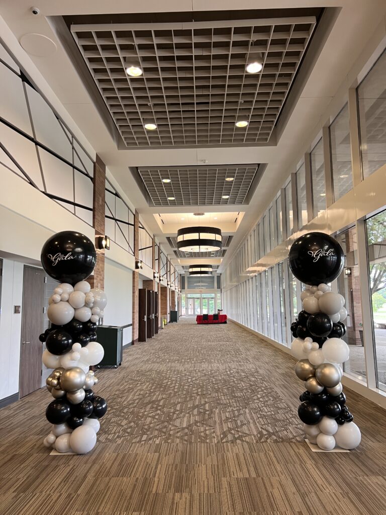 Balloon columns frame a spacious hallway adorned with modern lighting and furniture, setting a festive tone for an event or gathering.