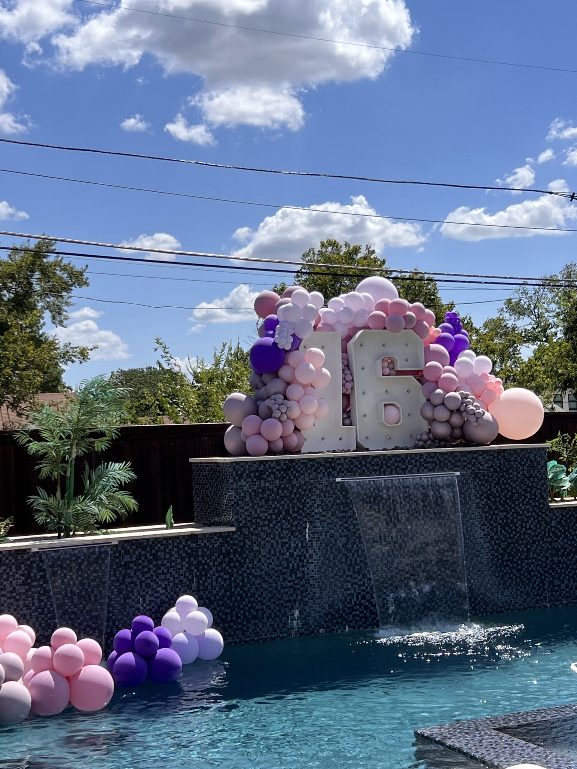 A vibrant poolside setup featuring large "16" letters adorned with pink and purple balloons