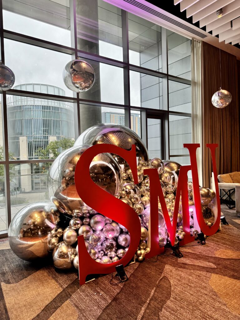 Large "SMU" letters are surrounded by colorful, metallic balloons in a modern venue, highlighting a branded event atmosphere.