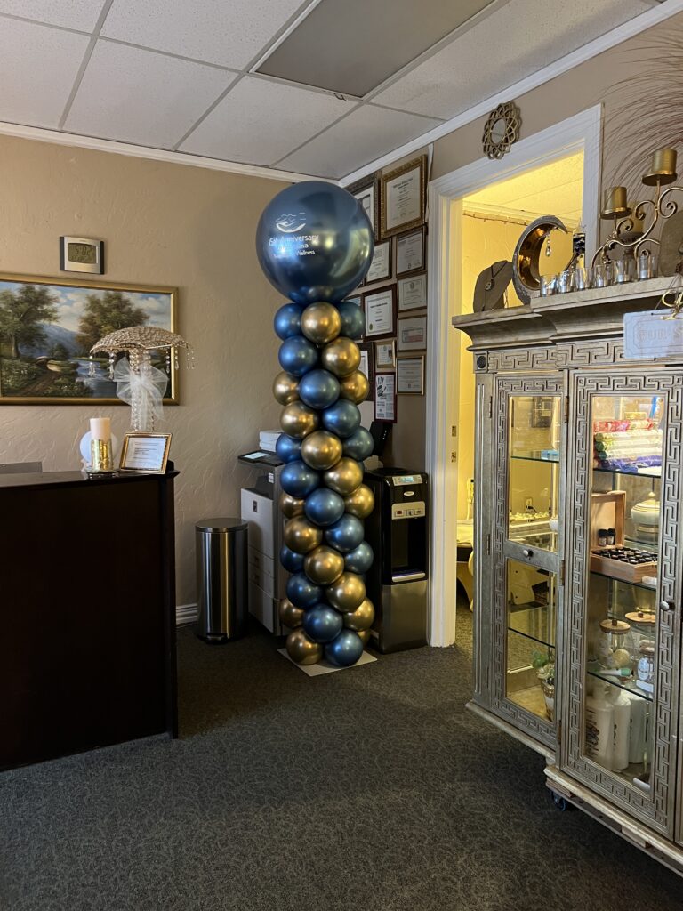 A celebratory balloon column in blue and gold, with a large balloon on top, decorates a professional office space.