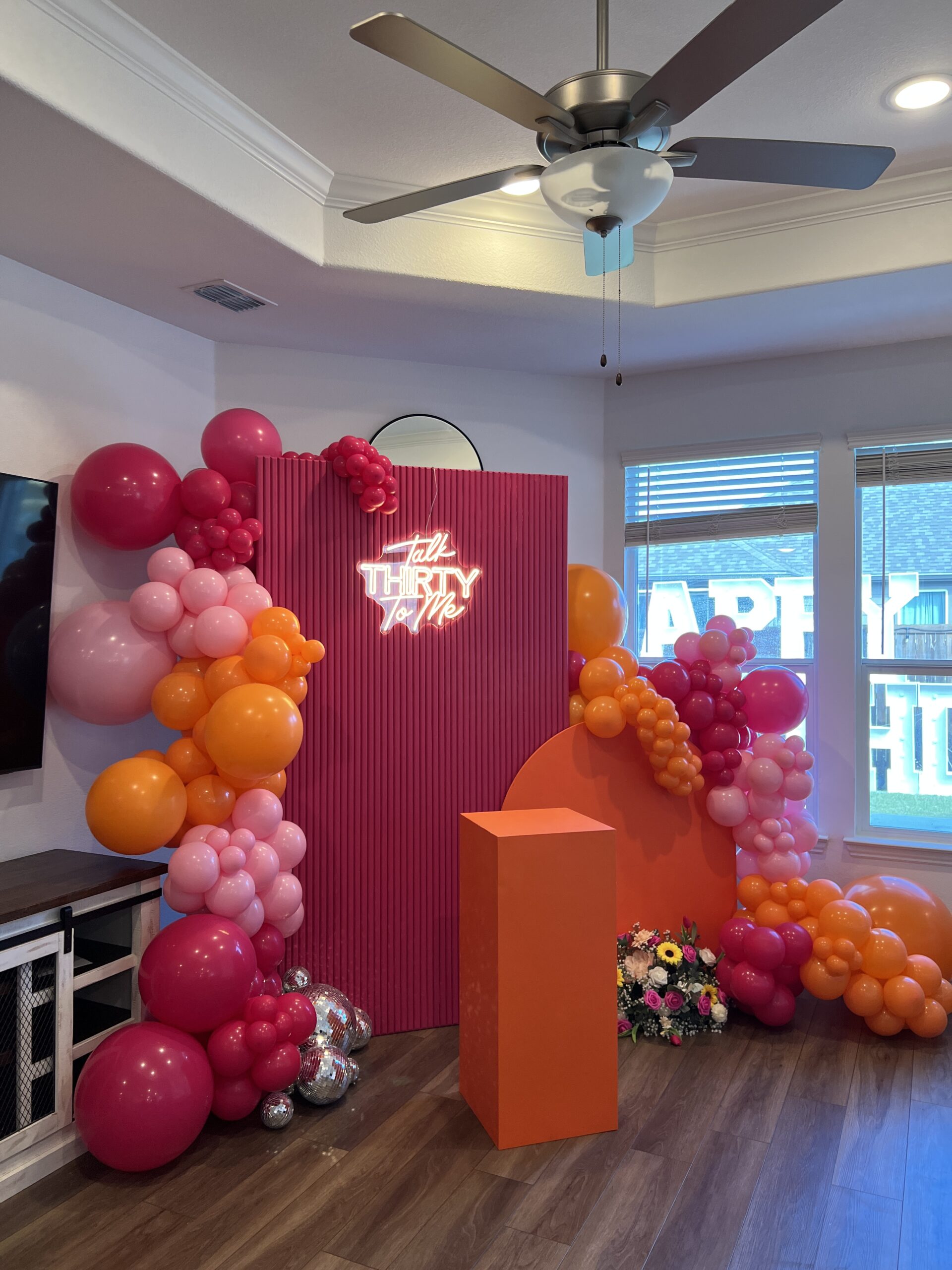 A colorful party backdrop featuring a neon sign reading "Talk Thirty to Me," surrounded by vibrant balloons in pink, orange, and yellow.
