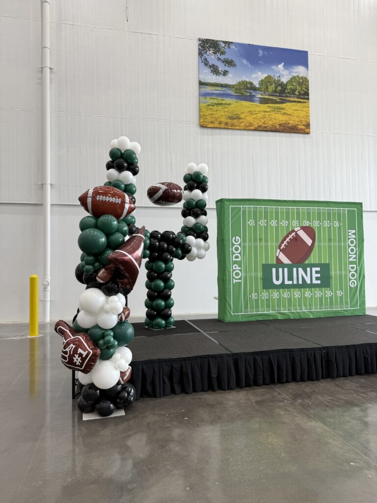 Football-themed balloon decorations on a stage, featuring a goal post and footballs. Relevant for a sports event or celebration.